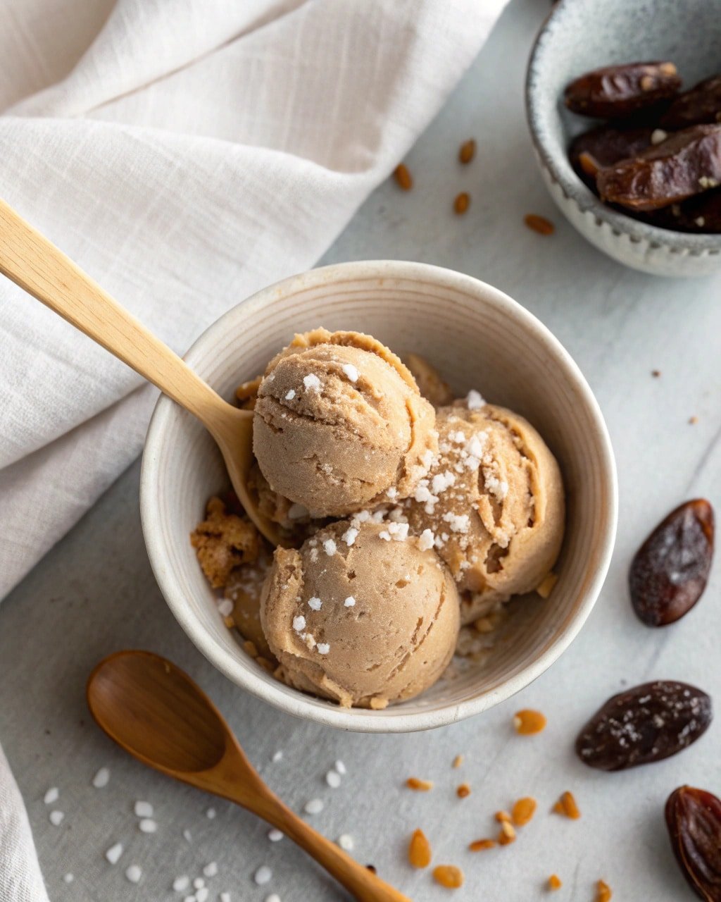 Top-down view of Salted Miso Date Creami in a ceramic bowl with flaky sea salt and wooden spoon